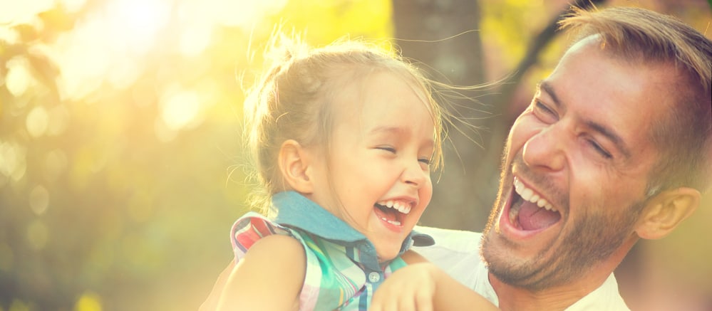 A dad carrying his young daughter outside, both are laughing