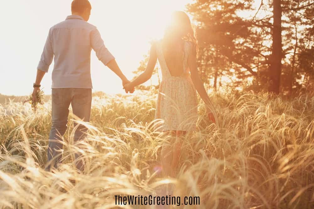 A young man and woman standing in field holding hands