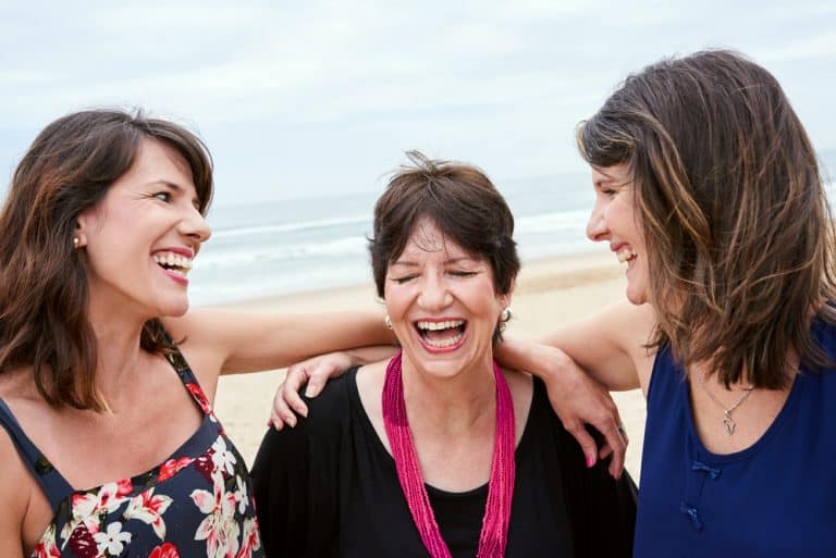a mom and her 2 daughters laughing on the beach