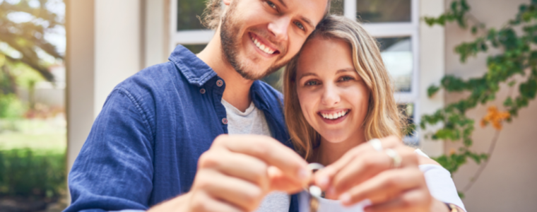 Young couple holding keys to new home in background